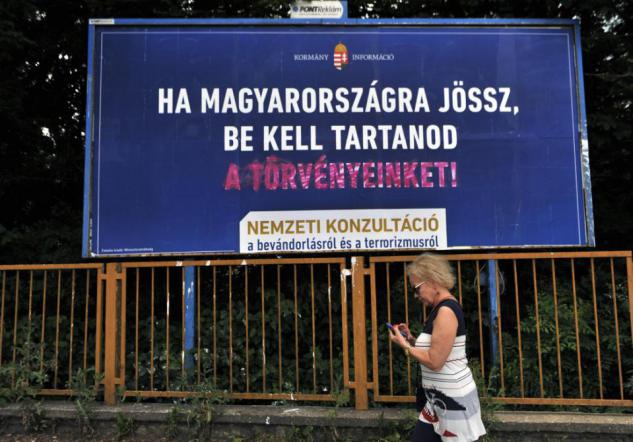 FOR STORY: HUNGARY BILLBOARD BATTLE - A woman is walking in front of a vandalized anti immigration billboard reading If you come to Hungary, you have to respect our laws! in Budapest, Hungary, on June 15, 2015. Hungarys central-right government has launched a controversial billboard campaign against immigration while UNHCR introduced its counter campaign highlighting successful refugee stories.  (AP Photo/Bela Szandelszky)